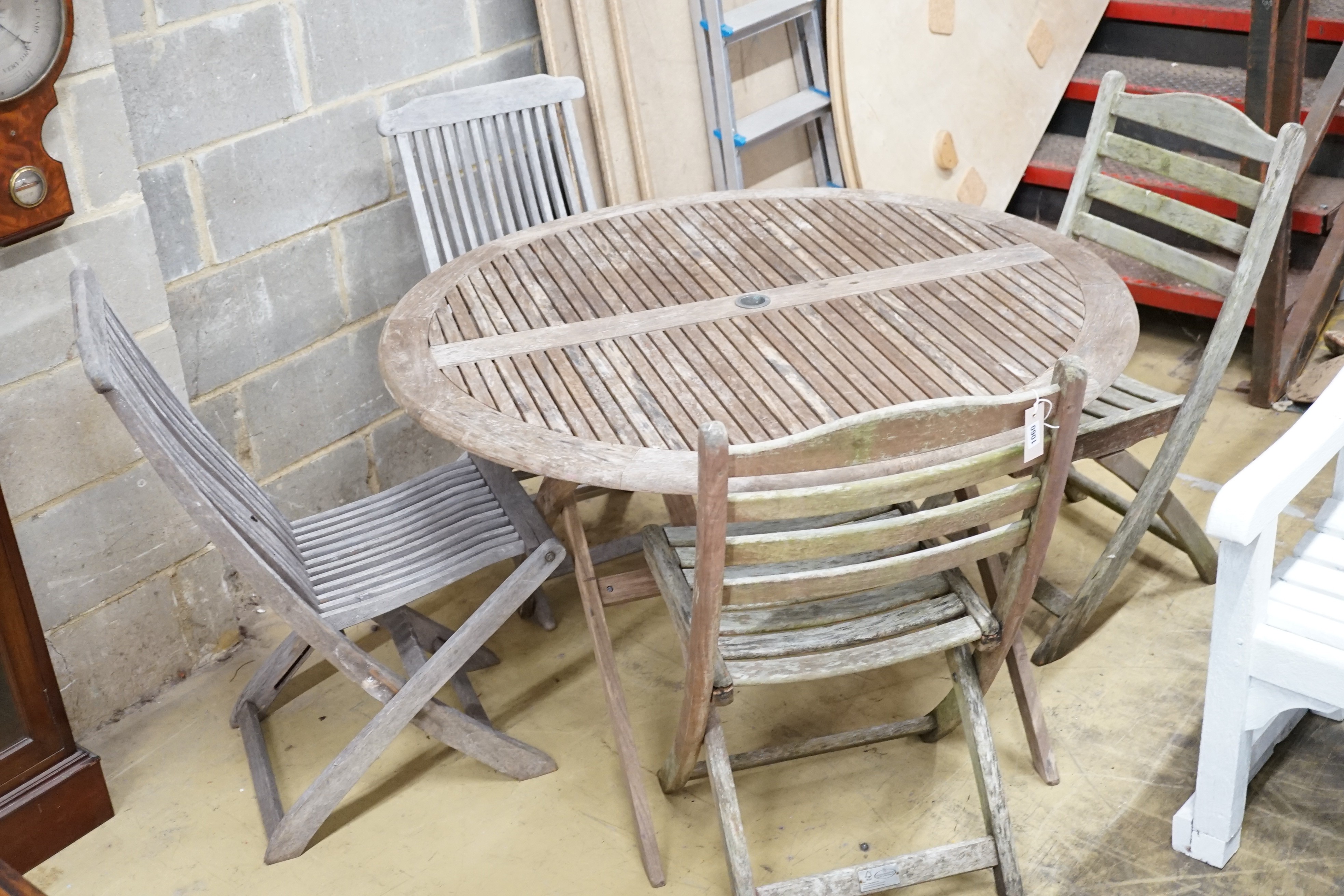 A weathered teak circular folding garden table, diameter 116cm and two pairs of folding chairs
